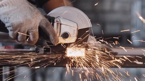 Manufacturing Plant Man Worker Cutting the Part of Metal Detail with Angle Saw Bright Sparkles