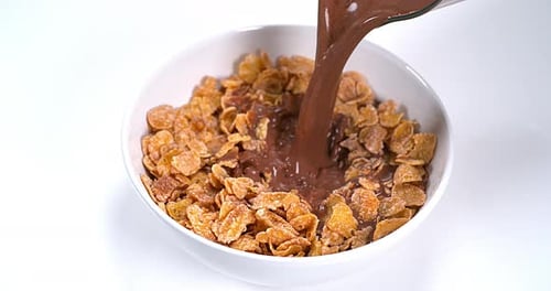 Pouring Chocolate Milk onto Crunchy Cornflakes in White Bowl