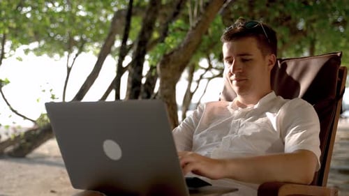 Der nachdenkliche Geschäftsmann schaut zum Strand und arbeitet weiter am Laptop