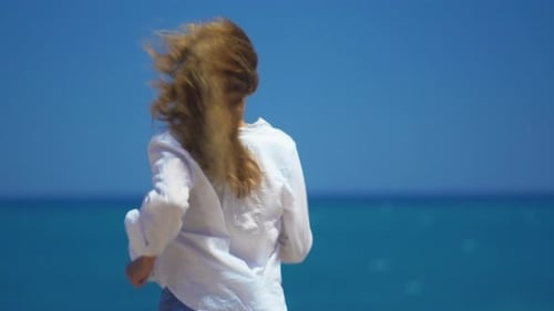 A Young Girl Runs Up To the Cliff Above the Beautiful Sea. Beautifully Develop Hair in the Wind