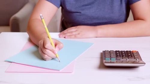 Woman is using a calculator to calculate and write down her monthly accounting expenses at home.