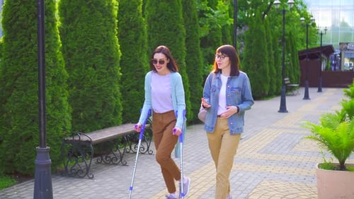 Two Women Walking in Park, One Using Crutches