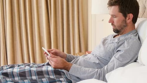 Man Relaxes in Bed, Using Tablet Device