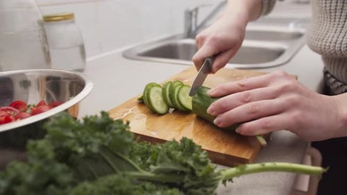 Person Slicing Cucumber on Cutting Board