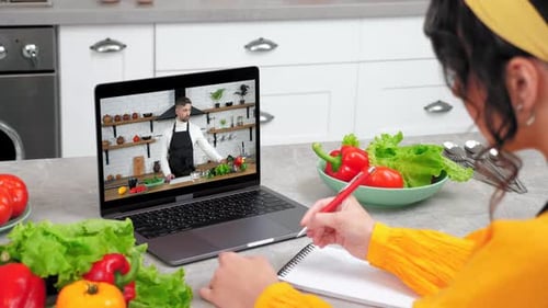 Mujer en cocina Estudiar Ver seminario web en línea Escuchar el profesor escribe en un cuaderno