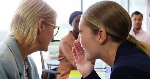 Two businesswomen whispering