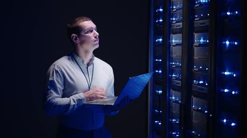 Young Man Monitors Servers with Laptop in Data Center