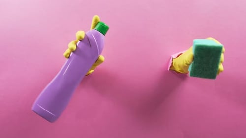 Hands in Gloves Hold Cleaning Supplies on Pink