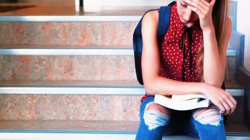 Sad schoolgirl sitting alone on staircase