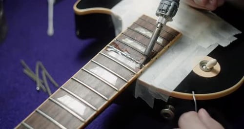 Luthier calienta los trastes de la guitarra soldando el hierro antes de refrescar los preparativos del artesano de la guitarra para