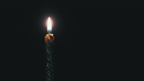 Eine einzelne Kerze wird auf einem schwarzen Hintergrund angezündet. Kerzenflamme im Dunkeln.