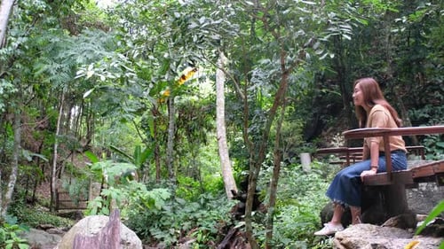 Une belle jeune femme asiatique assise et jambes suspendues dans la forêt