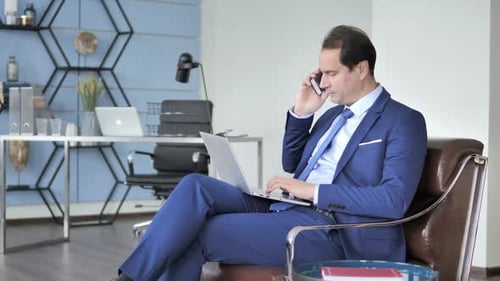 Man in Suit Using Laptop and Talking on Phone