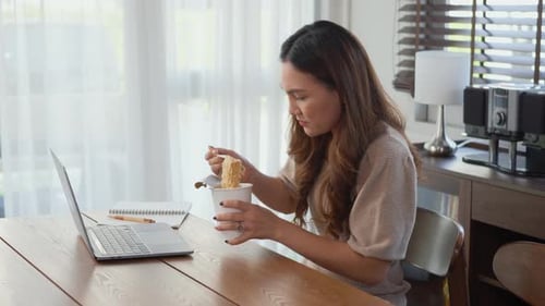 Woman Typing and Eating Noodles at Home