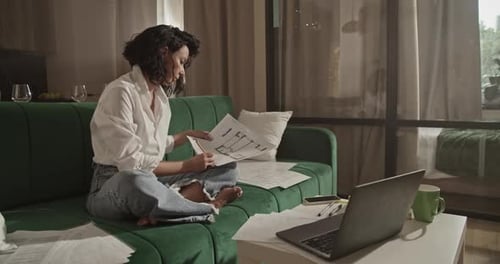 Woman Reviews Architectural Plans at Home on Couch
