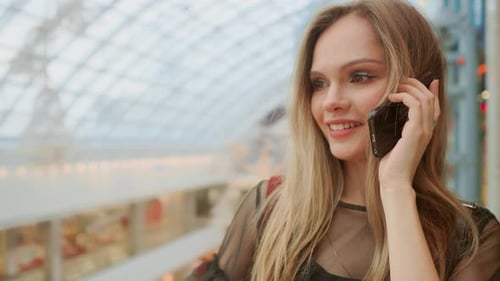 Beautiful Girl Talking on Smartphone and Sitting with Shopping Bags in Mall