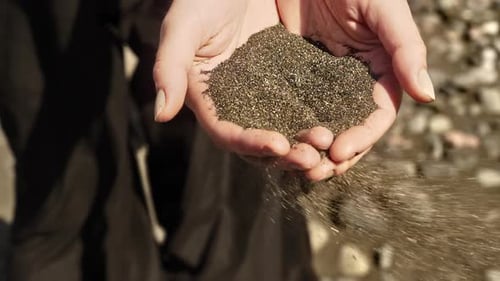Woman Holds Dark Sand at the Beach