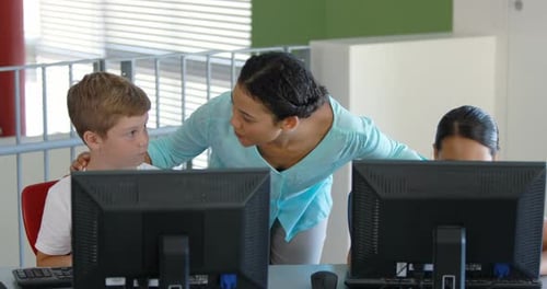 Teacher assisting schoolgirls in learning computer