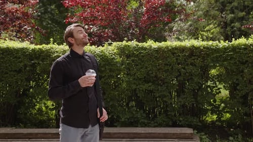 Man Enjoys Iced Coffee in Green Urban Park