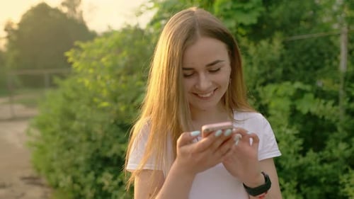Portrait of a Beautiful Woman Typing on a Mobile Phone in the Park