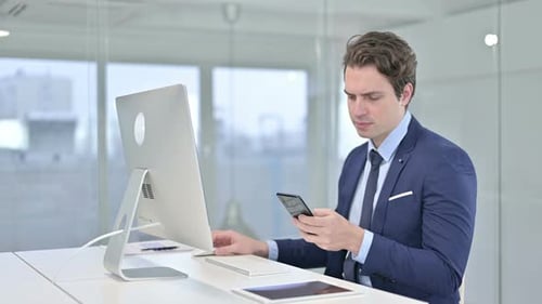 Young Adult Using Phone and Computer at Desk