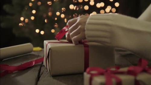 Person Wrapping Christmas Gift with Red Ribbon