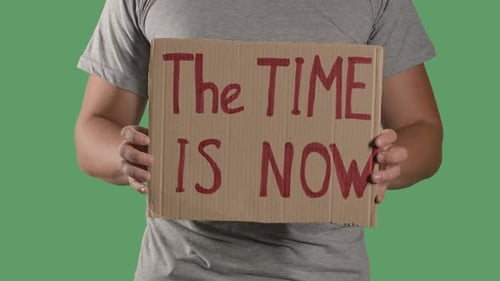 Person Holding The Time Is Now Cardboard Sign