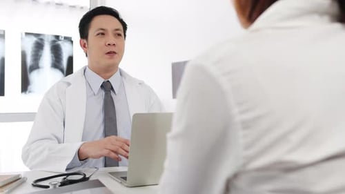 Asia male doctor great news talk symptoms with female patient sitting at desk in health clinic.