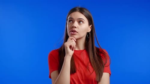 Thinking Woman Looking Up and Around on Blue Studio Background