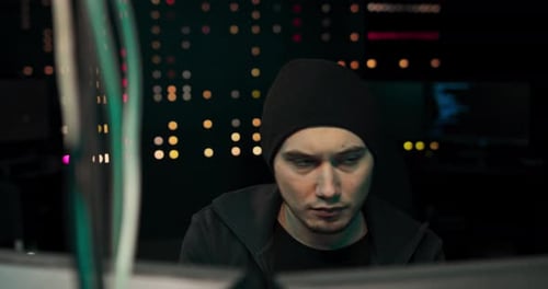 Hacker in Headset and Eyeglasses with Keyboard Hacking Computer System or Programming Hideout Place