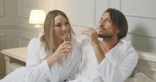 Affectionate Couple Toasting with Champagne Lying on Their Bed. Hotel, Travel, Relationships and