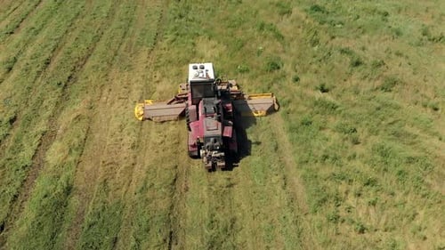 Luftaufnahme einer landwirtschaftlichen Maschine, die an einem sonnigen Tag auf einer Wiese saftiges Gras mäht