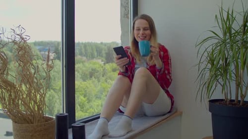 Woman Using Smartphone and Drinking Coffee Indoors