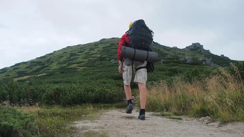 Tourist with a Backpack Climbing Up Along the Stone Mountain Trail on the Hill
