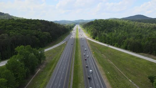 Cars and trucks driving on a divided highway. The camera is from a drone perspective and does note w