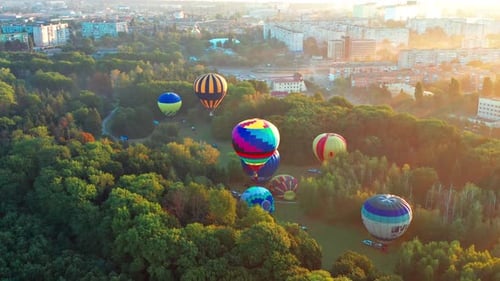 Beautiful sunbeams illuminate the balloons that fly over the park, green trees.