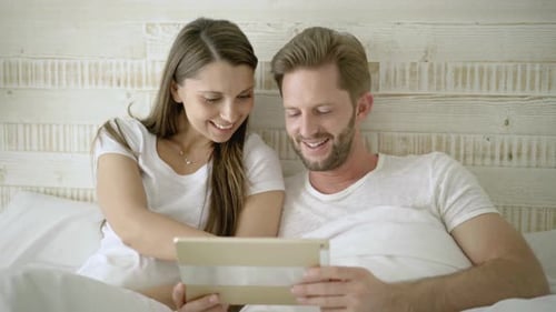 Smiling Couple Enjoying Tablet Together in Bed