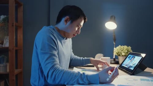 Asia freelance businessman video call meeting on tablet computer assignment paperwork.