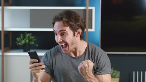 Excited young man looks at phone and celebrates