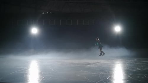 Une jeune patineuse artistique se produit sur une patinoire dans l'obscurité Une petite figure se déplace contre