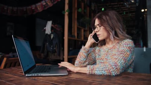 Happy Young Woman Sits with Phone and Computer at the Table
