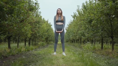 Woman Exercising Outdoors Doing Squats in Orchard