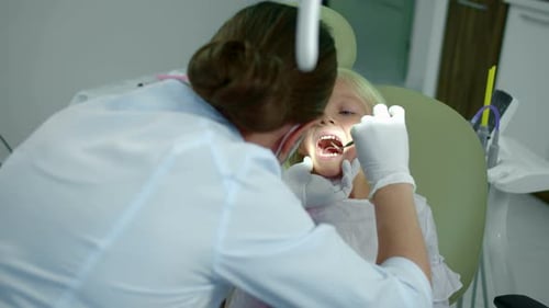 Dentist Examining Young Girl's Teeth in Clinic