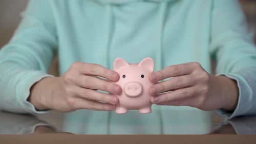 Female hands putting a piggy bank on the table. Money saving concept.