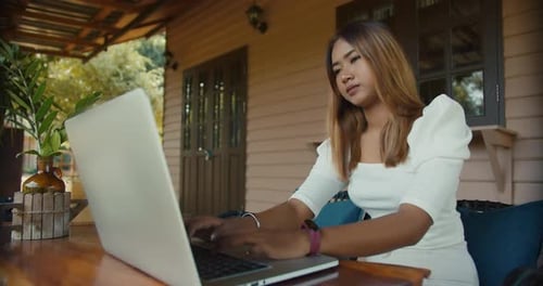Asiatisches Mädchen im weißen Kleid sitzt auf der Terrasse und genießt die Aussicht und benutzt mittags Laptop