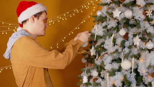 Man Decorates Christmas Tree with Ornaments at Home