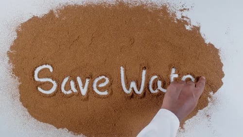 Hand Writes 'Save Water' in Brown Particles