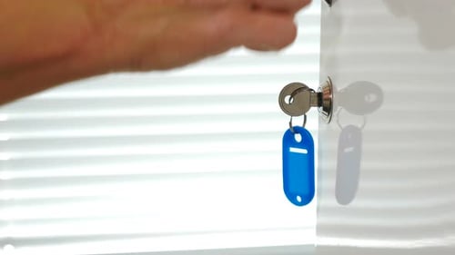 Female Hand Using Key with Blue Keyholder To Close Metal Door in White Shelf. Hand Closes Steel Cell