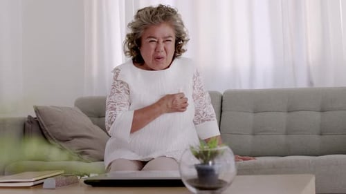 Asiatische ältere Frau Brustschmerzen aufgrund von Herzerkrankungen auf dem Sofa im Wohnzimmer.