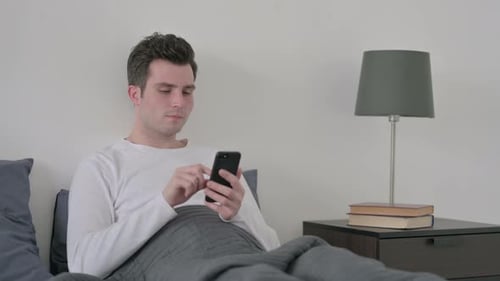Man Using Smartphone in Bed in Bright Room